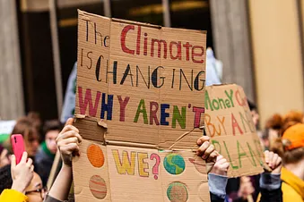 Schilder mit einer Parole auf einer Demonstration: “The Climate is changing. Why aren’t we?” und “Money can’t buy a new planet.”