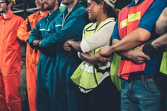 Arbeiterinnen und Arbeiter in Arbeitsmontur, die sich die Hände halten