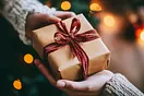 üUbergabe eines Geschenks von Hand zu Hand. Das Geschenkpaket ist mit einer Masche umgeben.